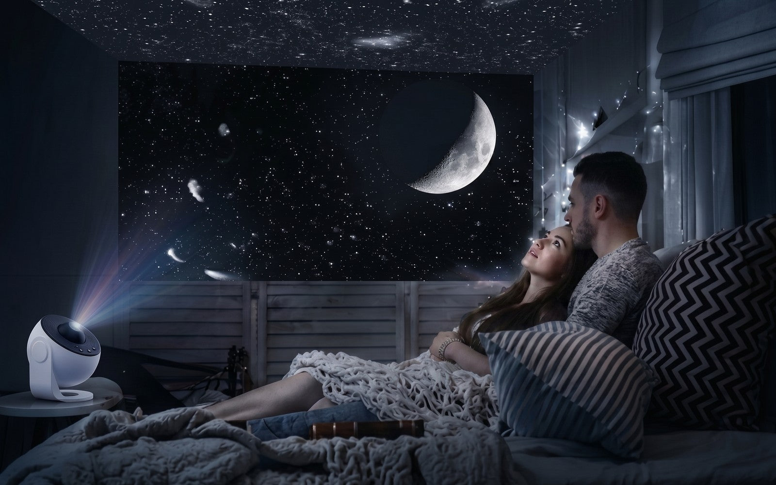 Couple allong&eacute; dans un lit, la Lune et un ciel &eacute;toil&eacute; projet&eacute;s sur le mur