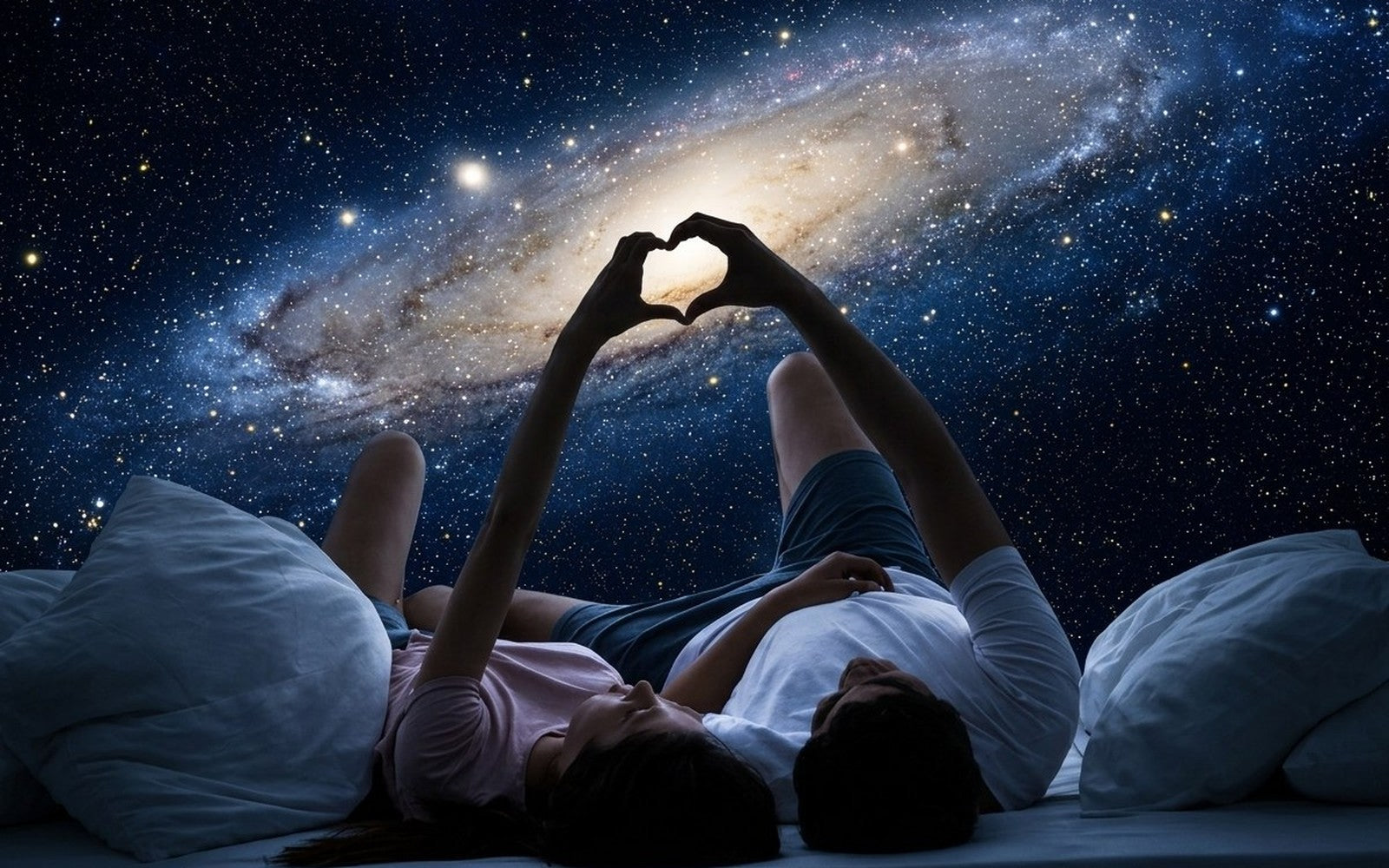 Couple allong&eacute; formant un coeur avec les mains devant une galaxie projet&eacute;e